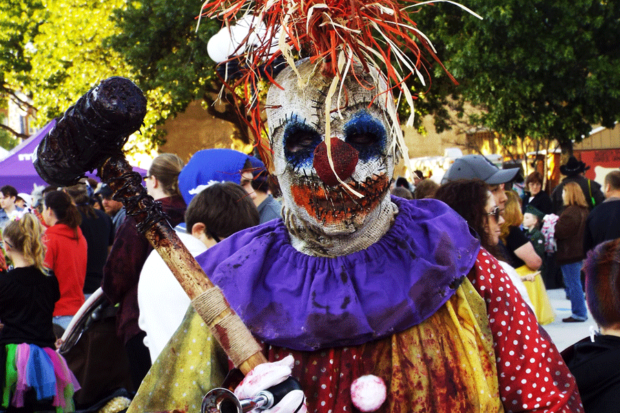 A zombie clown sports a bloodied sledge hammer wrapped in barbed wire. 